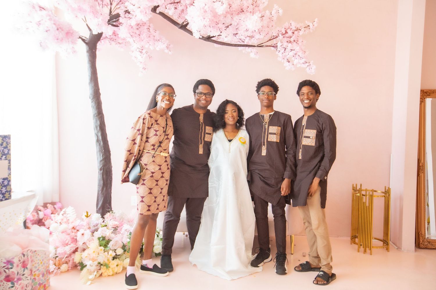 A group poses together under a pink cherry blossom tree at an indoor event space.