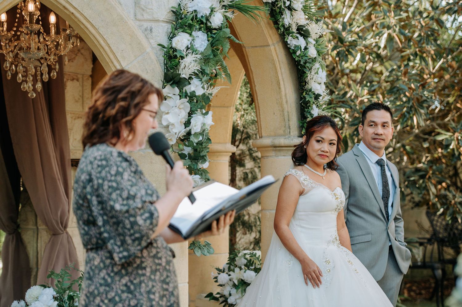 An outdoor wedding ceremony under an elegant archway decorated with greenery and flowers.