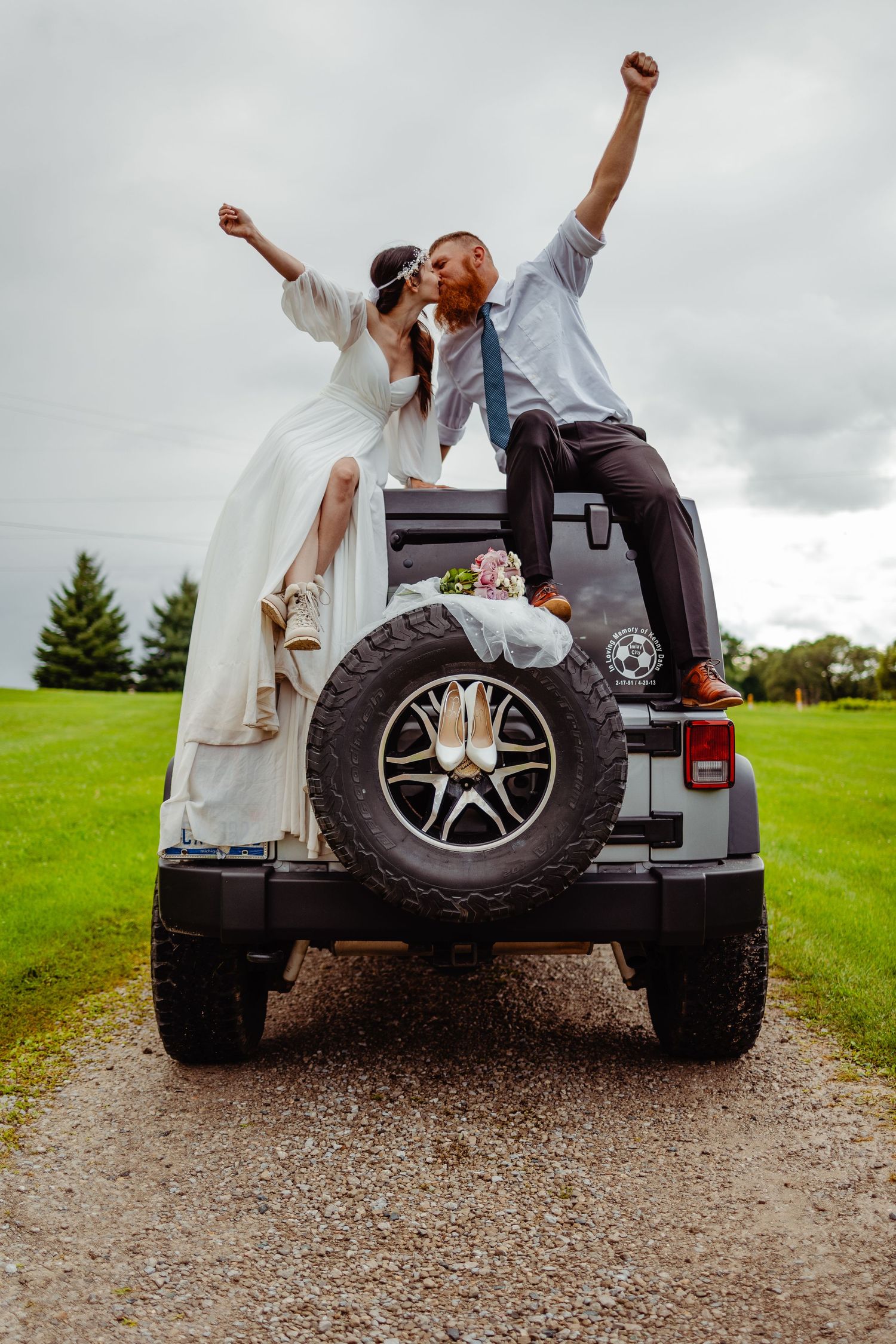 Wedding couple celebrating on back of Jeep with arms raised triumphantly.
