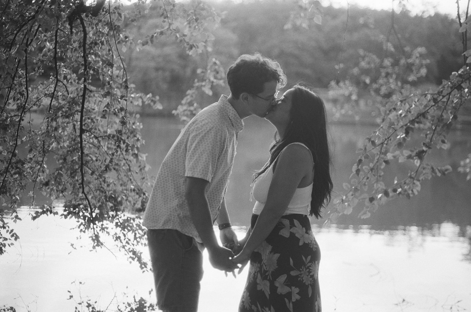 Couple sharing intimate moments by lakeside in soft natural lighting.