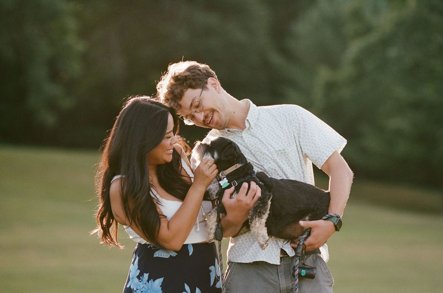 A couple plays with their small black puppy during an outdoor photo session.