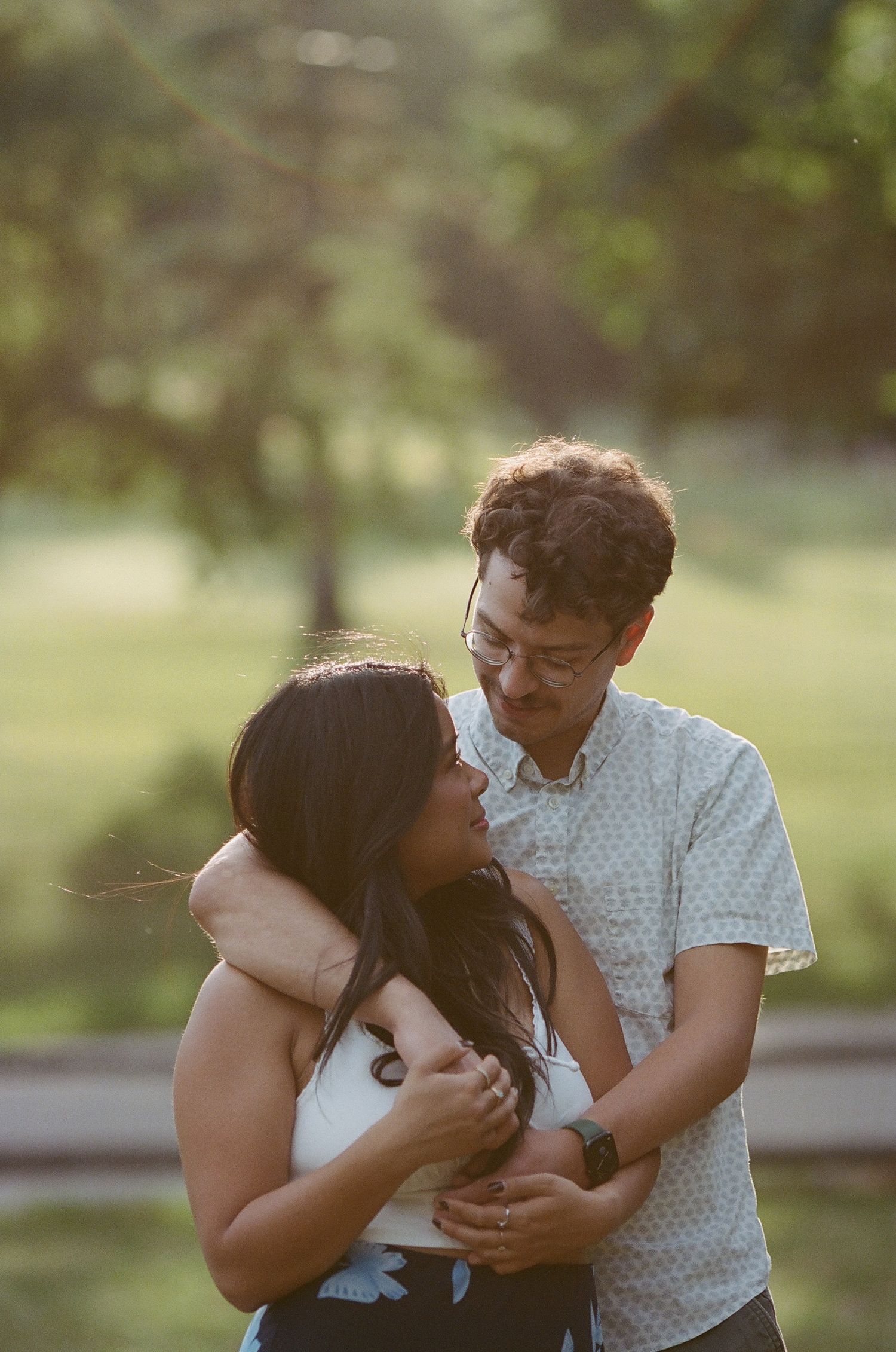 A couple shares a tender moment while holding their small black puppy in a park setting.