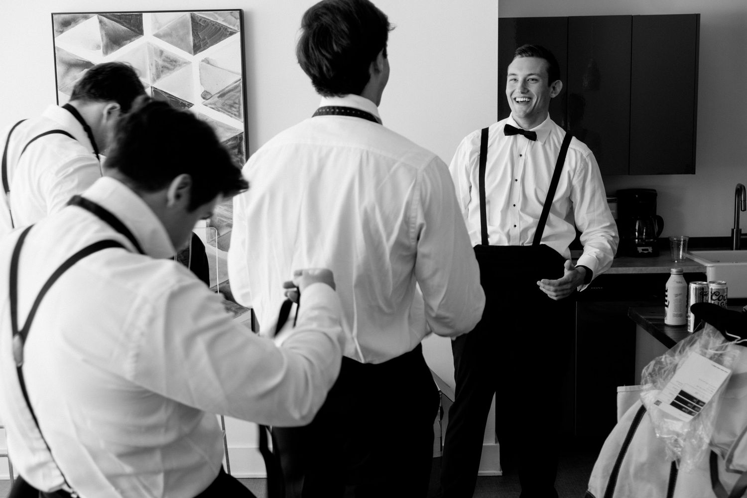 Black and white image of wedding preparation with photographers and groomsmen.
