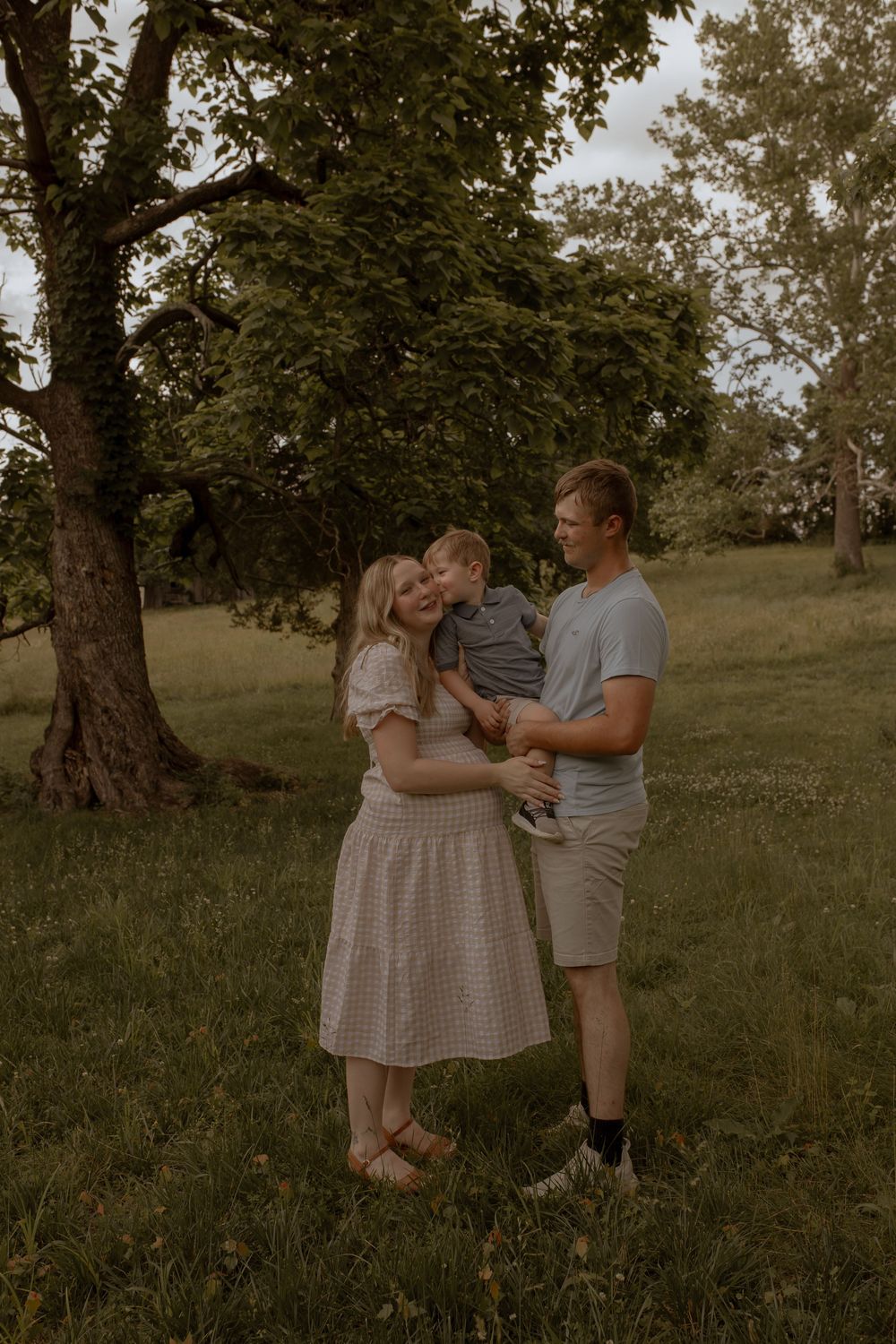A couple embraces in a serene park setting with trees in the background.