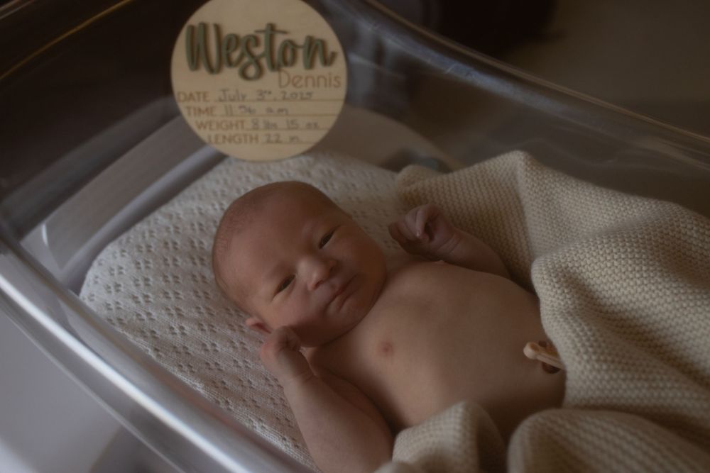 Peaceful sleeping newborn with wooden name sign in bassinet.