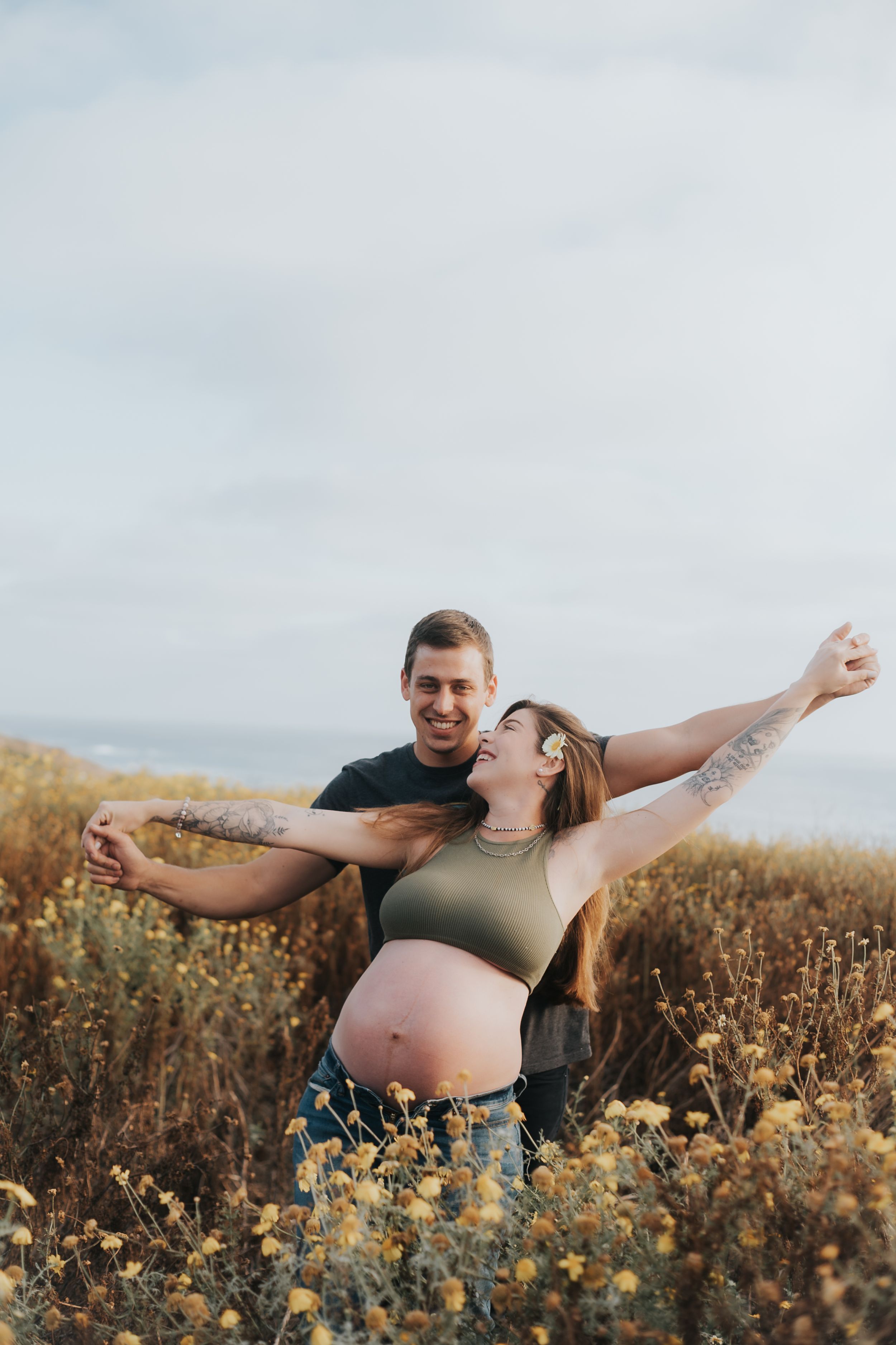 Expecting couple celebrating in a field of wildflowers during sunset.