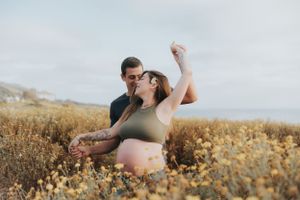 Couple sharing playful moment in golden field during maternity photoshoot.