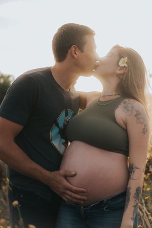 Romantic sunset maternity photo with couple embracing in wildflower field.