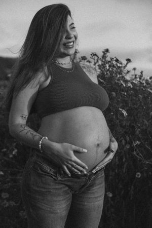 Black and white portrait of pregnant woman laughing in outdoor setting.