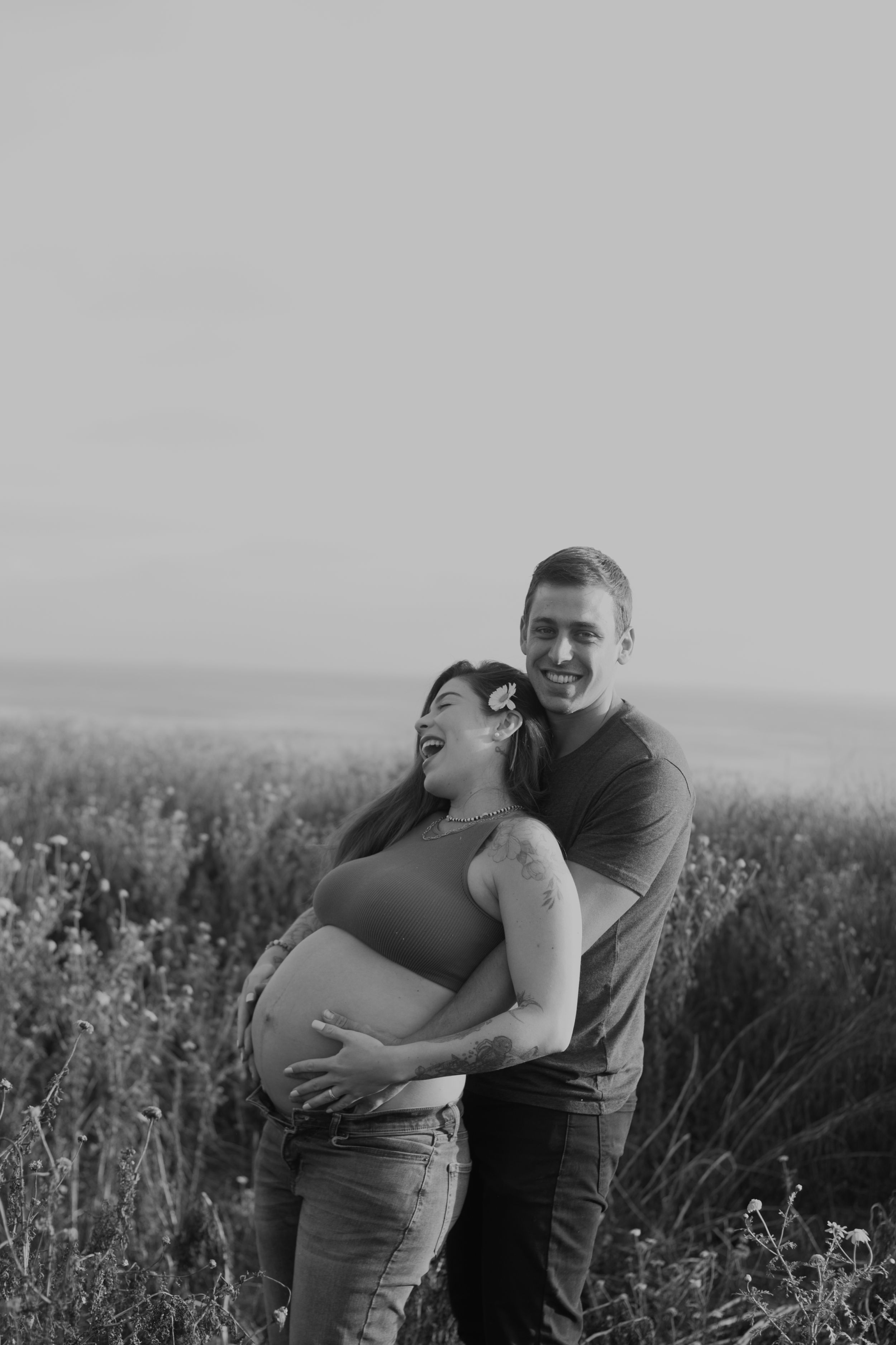 A joyful maternity photo of couple laughing together in a wildflower field.