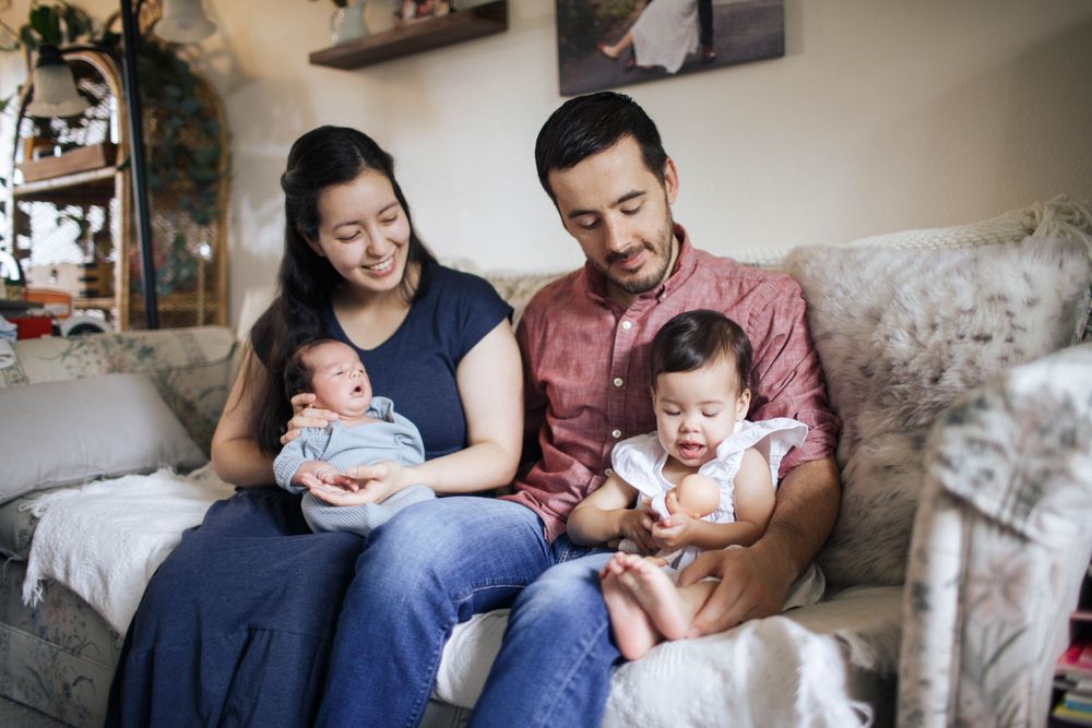 a mother and father sit on the couch with their newborn baby and their 18-month-old in Everett WA