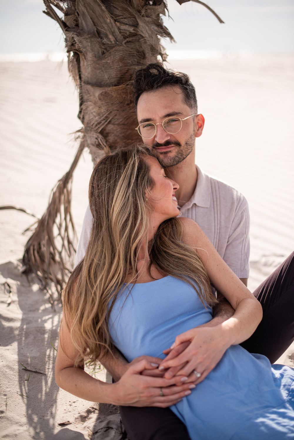 Romantic couple embracing under palm tree on sandy beach during sunset.