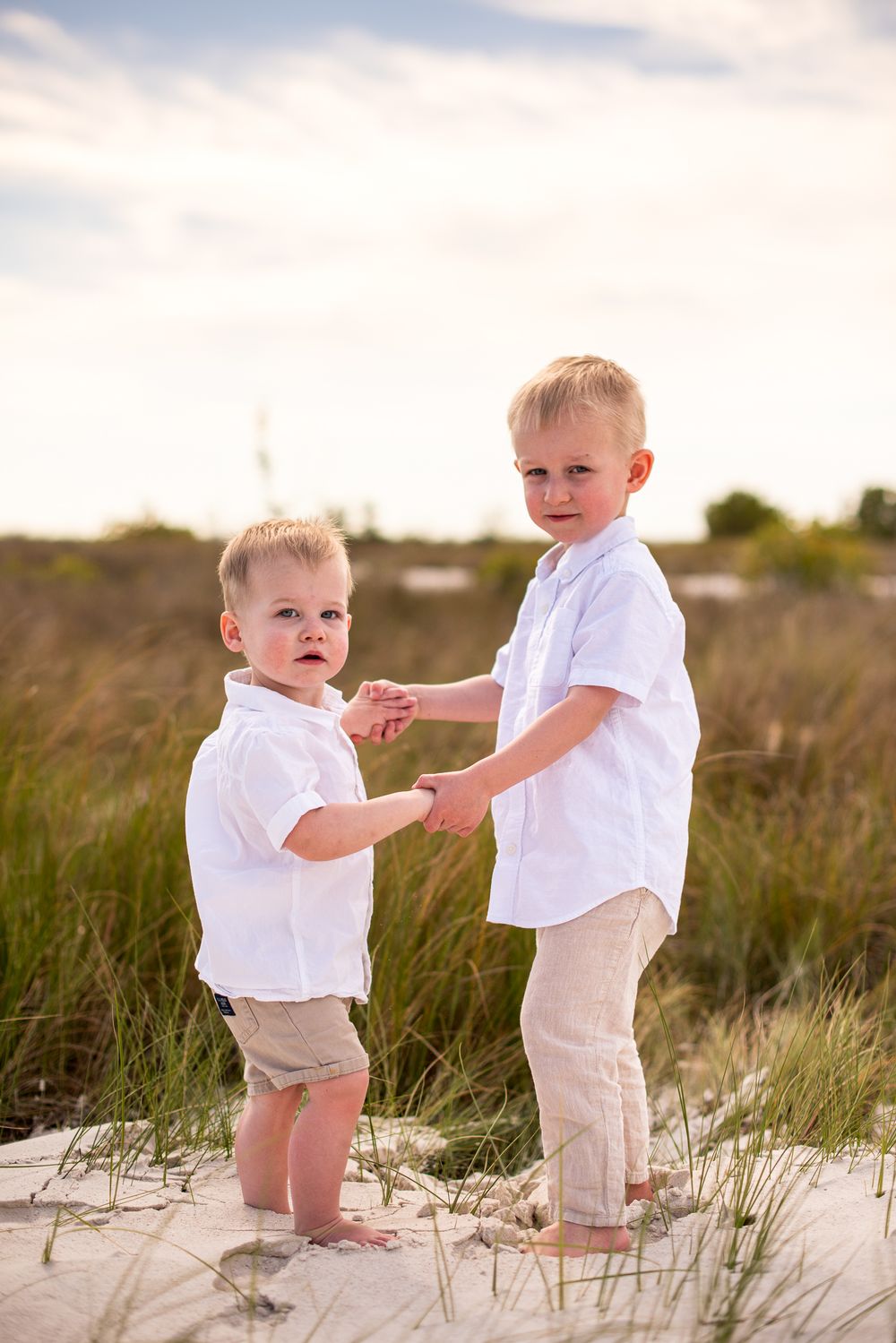 Two children in white outfits play together on a sandy beach dune at sunset.