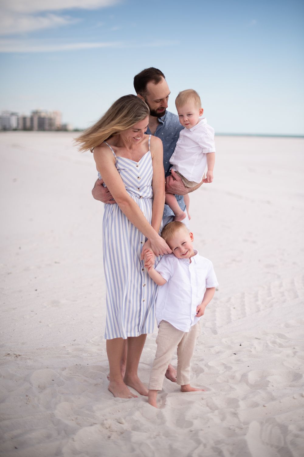 Family enjoying tender moment together on sunny beach with waves in background.
