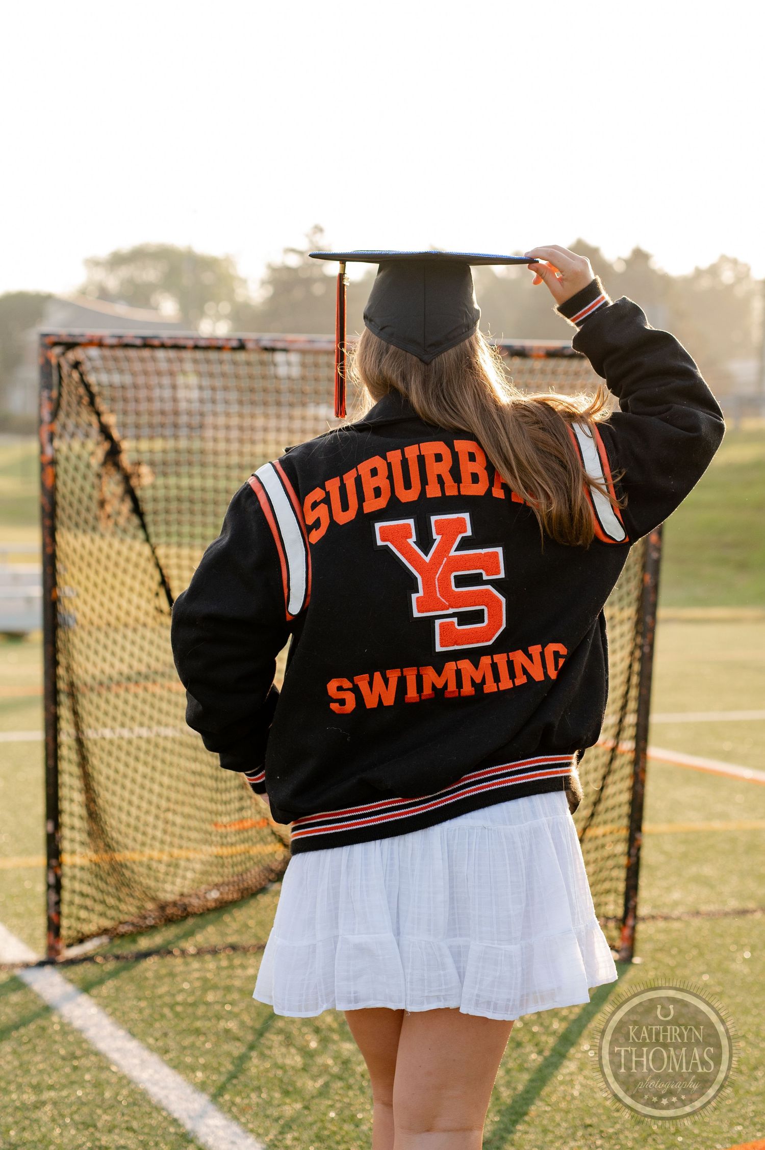 Suburban YS Swimming varsity jacket shown from behind on graduate with lacrosse goal in background.
