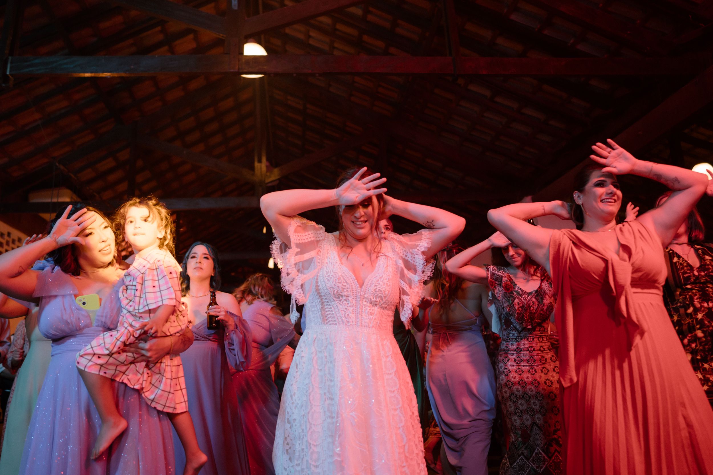 Group of people dancing with arms raised at a party under red lighting.