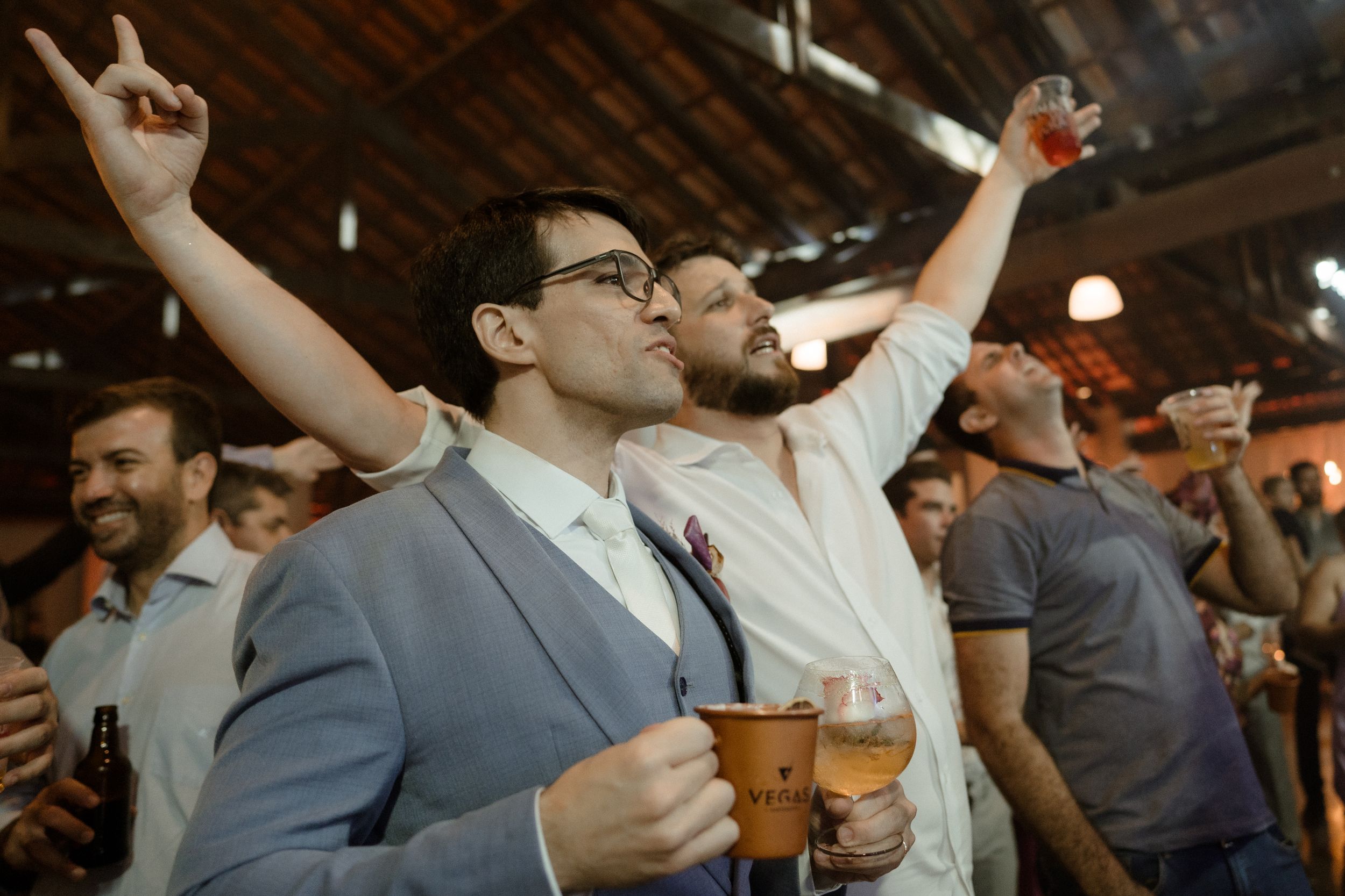 Party guests raise their drinks and cheer during an energetic wedding reception celebration.