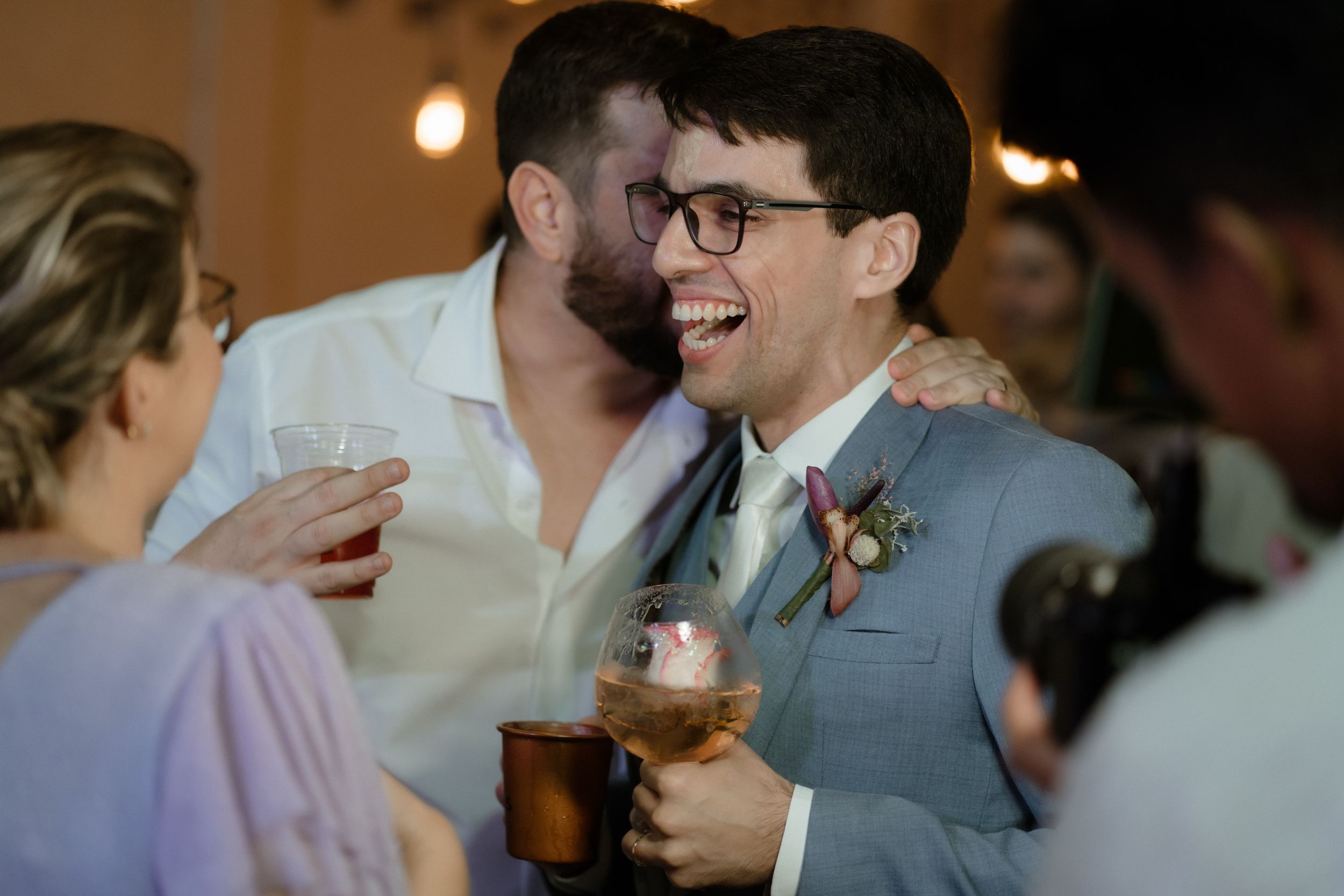 Wedding guests share laughs and drinks during a lively reception celebration.