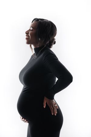 A pregnant woman in a black turtleneck dress poses in profile silhouette against a white background.