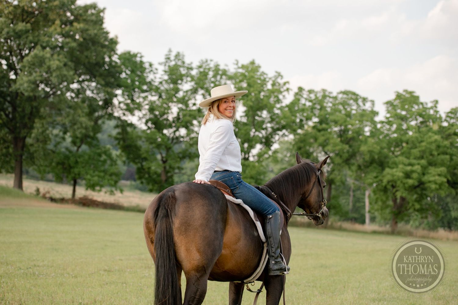 A majestic brown horse being ridden in an open field with trees in the background.