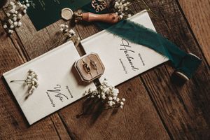 Elegant wedding stationery flat lay with wax seal, ring box, feather quill, and baby's breath on rustic wood.