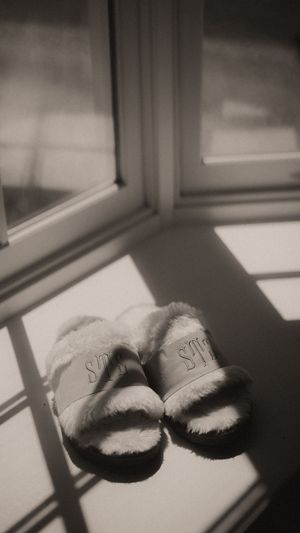 Fluffy white Victoria's Secret slide slippers resting on a windowsill in dramatic black and white natural light.