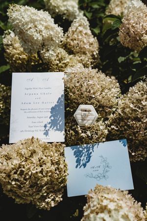 Wedding invitation suite for Arpana Uhale and Adam Hatter displayed on white hydrangeas with a hexagonal ring box.