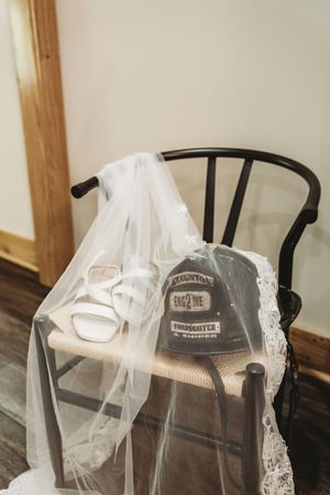 Bridal veil draped over a black chair with white heels and a firefighter Engine 2 cap, wedding detail shot.
