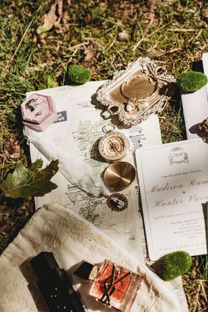 Vintage wedding flat lay with compass, map, invitation, ring box, and moss on grass.