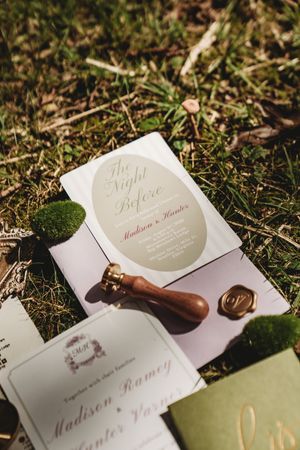 Elegant wedding stationery suite with wax seal stamp, invitation cards, and moss accents arranged on green grass.
