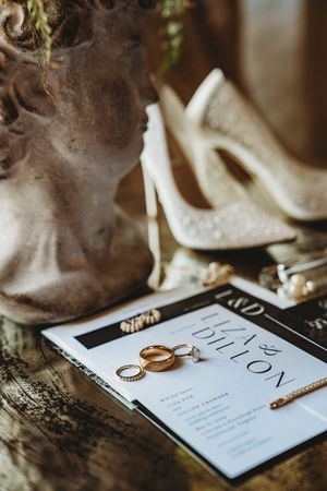 Gold wedding rings rest on an elegant black and white invitation card with delicate text details.
