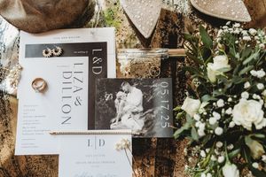 Elegant wedding details including floral arrangements, invitations, rings and decor laid out on rustic wooden surfaces.