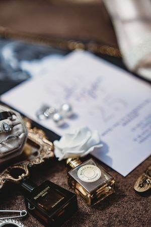 Wedding flat lay with perfume bottles, invitation, floral accents, and jewelry on a velvet surface.