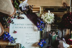 Elegant wedding invitation for Courtney Umstot and Nicholas Stole surrounded by florals, berries, and vintage books.
