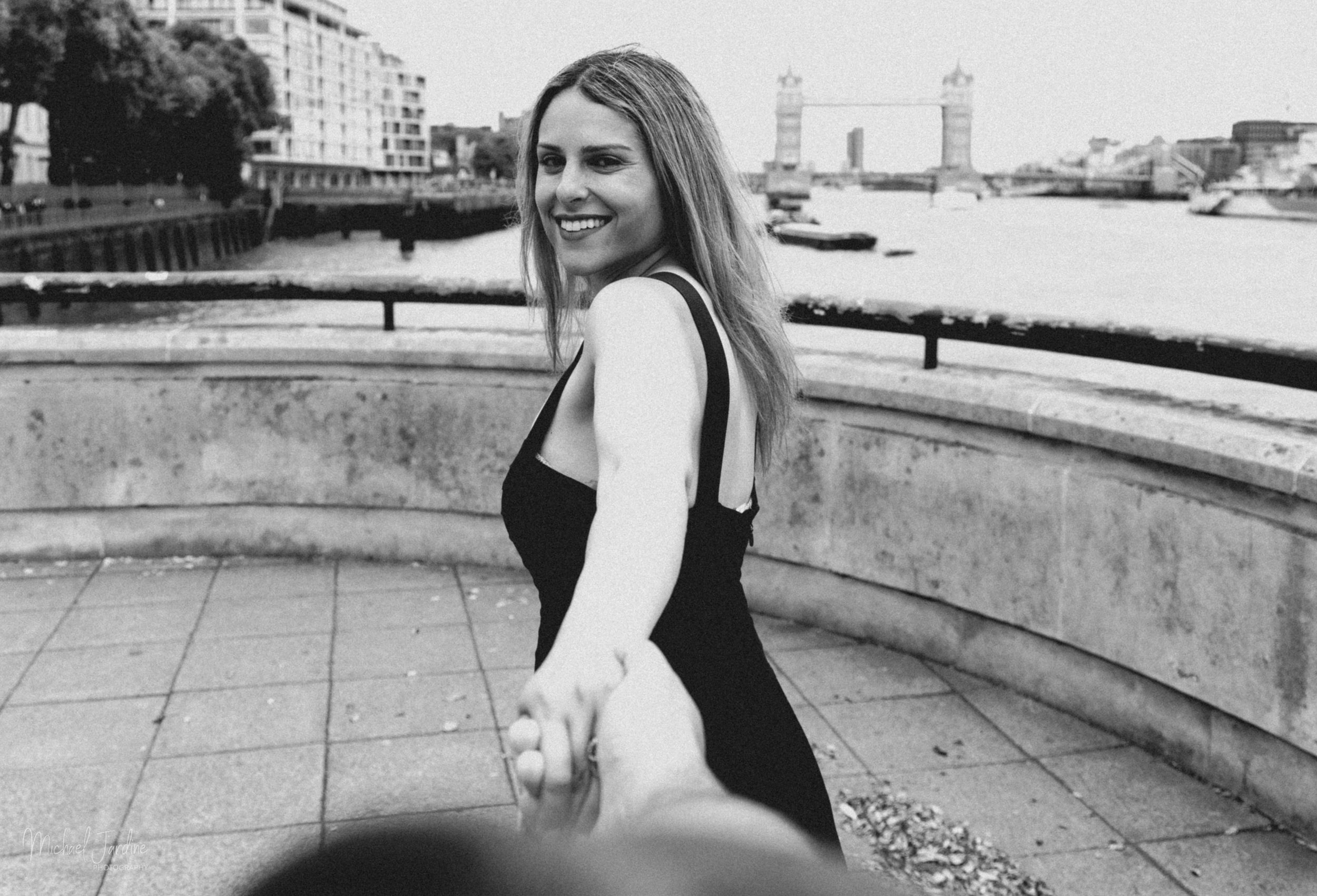 Black and white portrait of someone smiling and holding hands in an outdoor urban setting along South Bank London.
