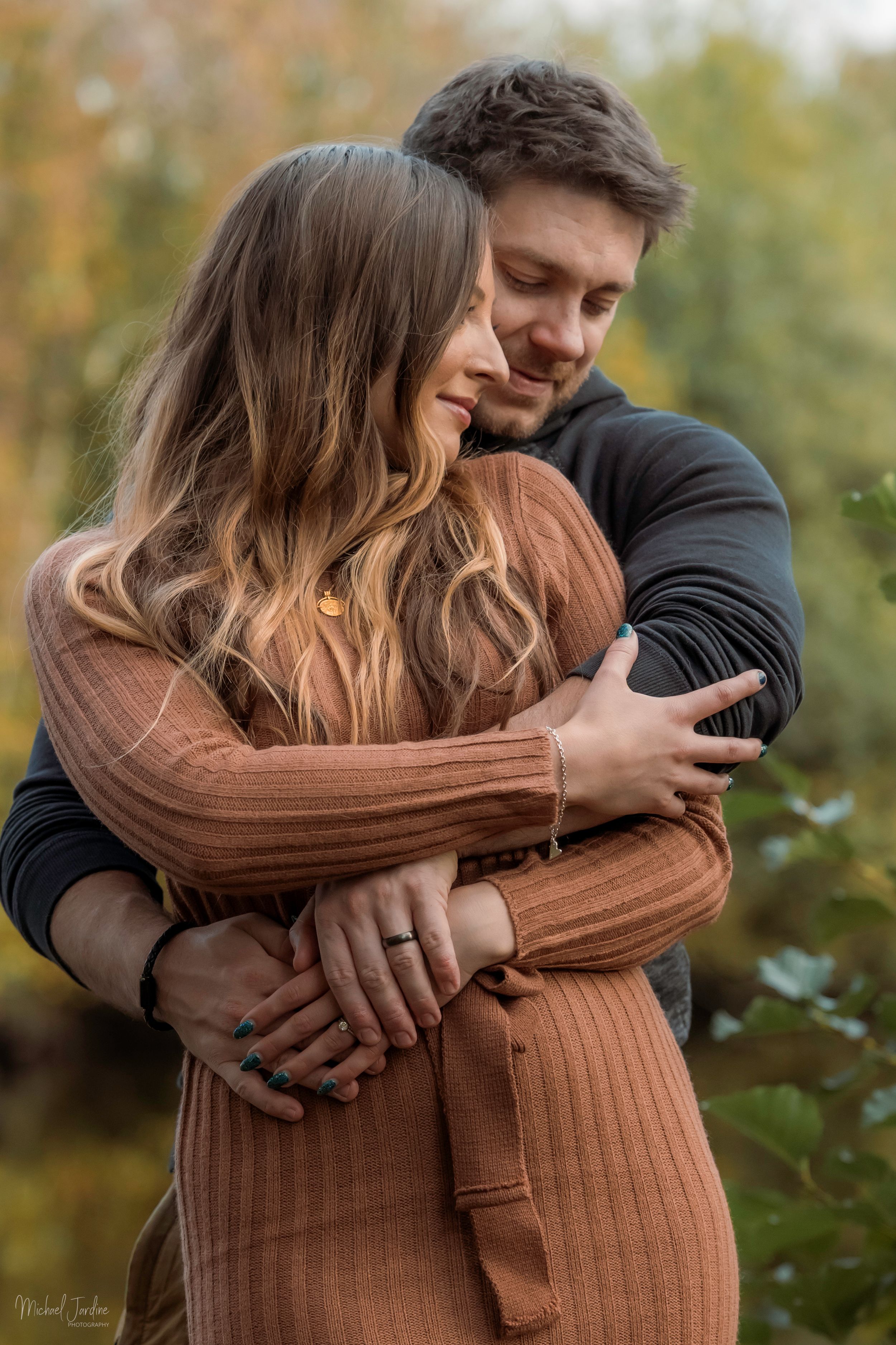 A couple embraces tenderly in a series of intimate outdoor photos with autumn foliage in the background.