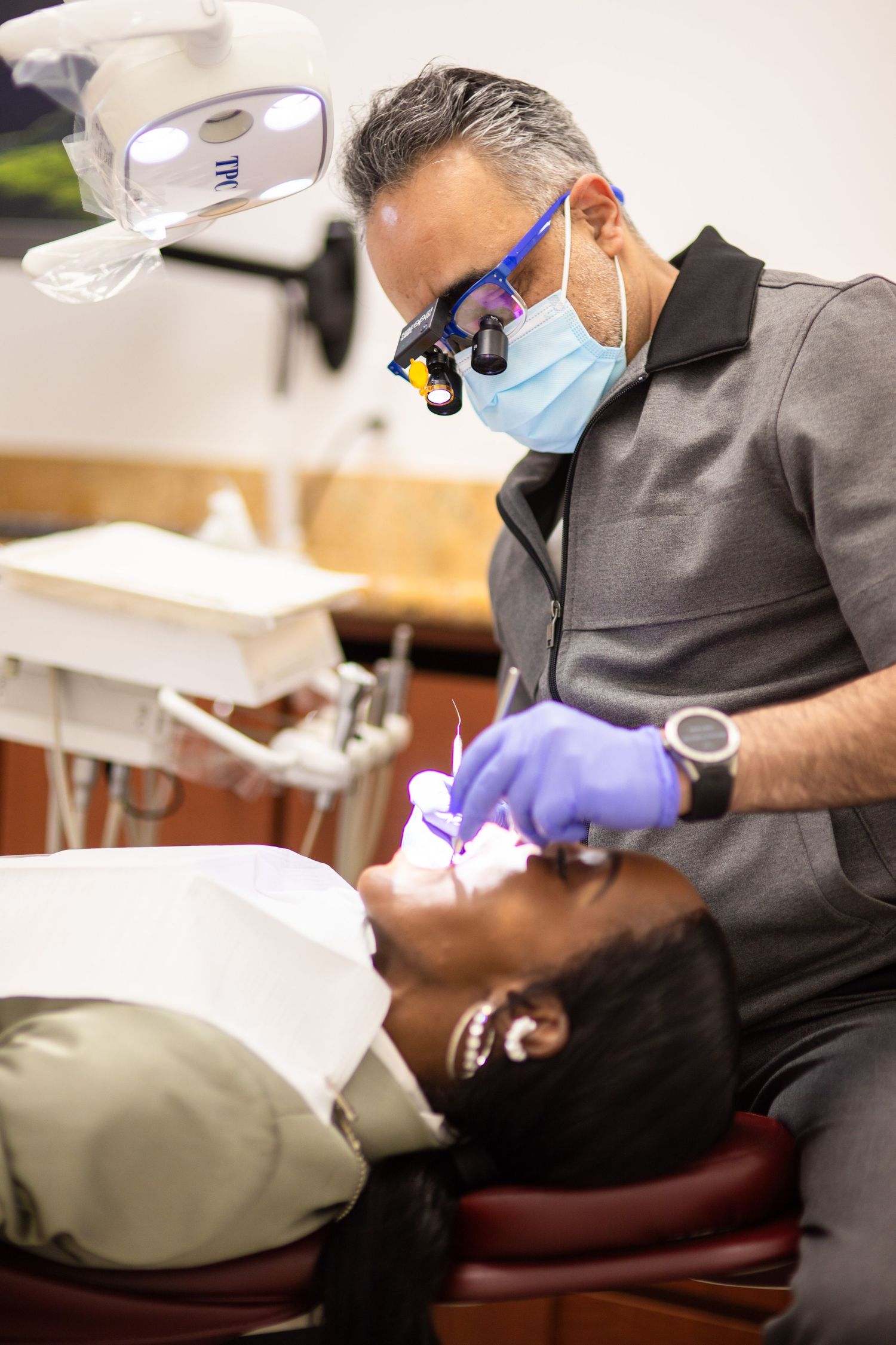 A dentist wearing protective gear performs a dental procedure in a clinical setting.