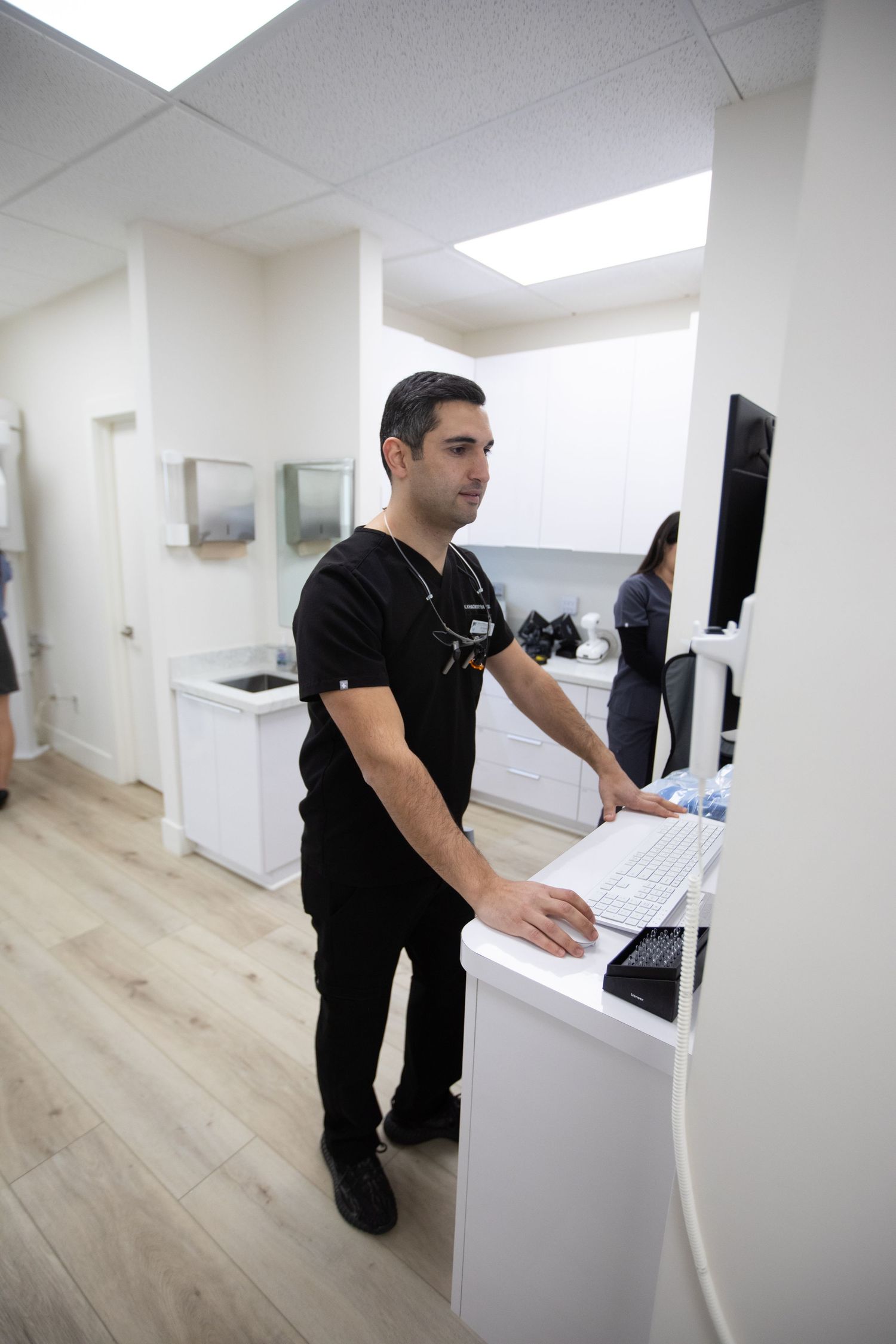 Healthcare worker in black scrubs working at computer station in modern medical office.