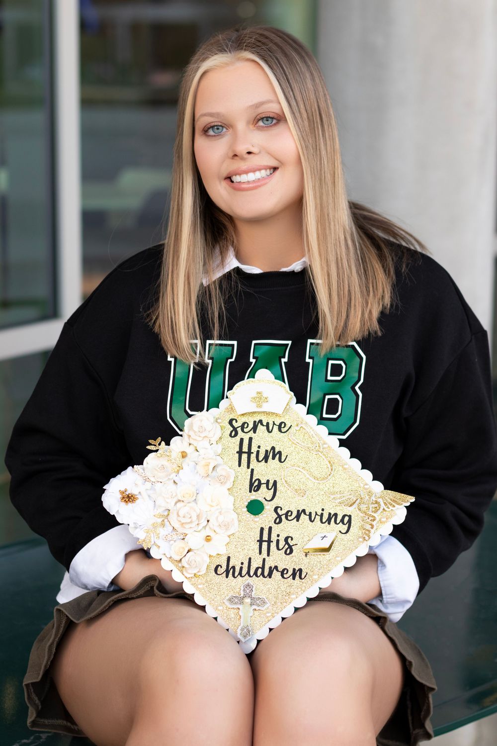 UAB graduate smiles holding decorated mortarboard cap reading serve Him by serving His children.