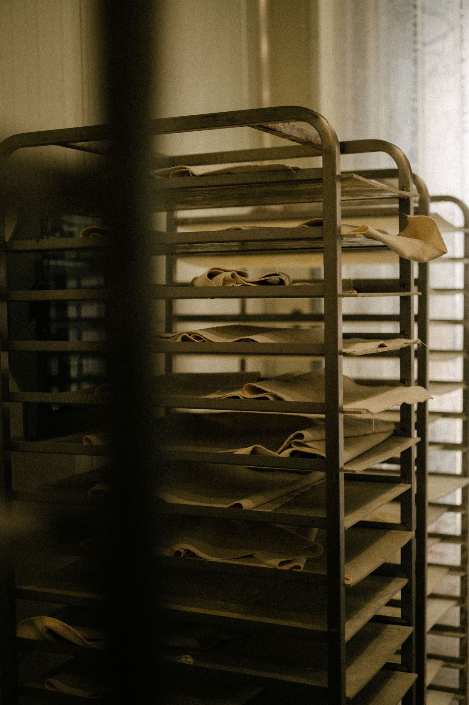 Industrial bakery racks with loaves in a dimly lit room.