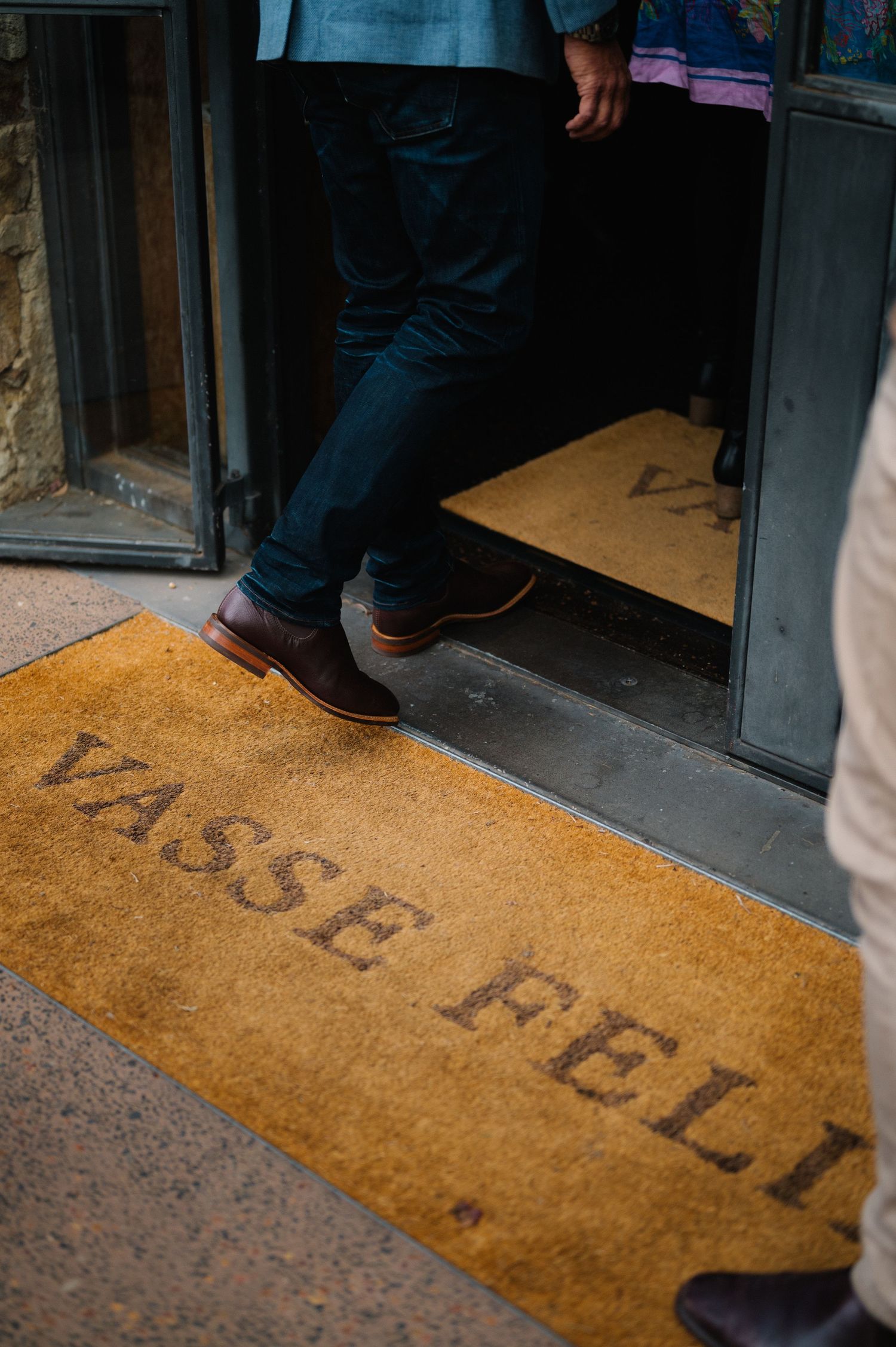 Close-up of someone stepping on a doormat that reads 'Vasse Felix'.