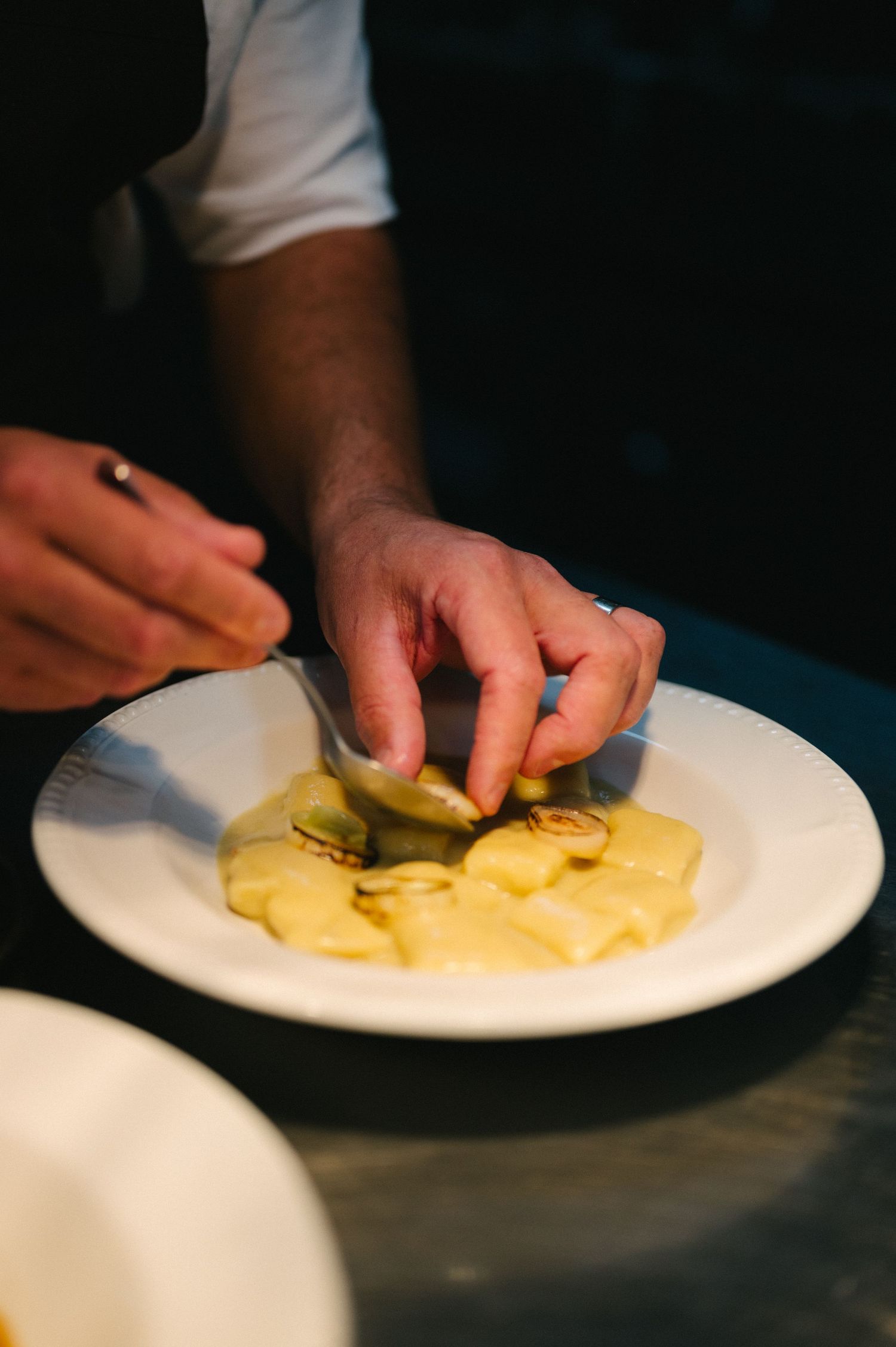 Chef's hands carefully plating sliced yellow fruit on white plates in a professional kitchen setting.