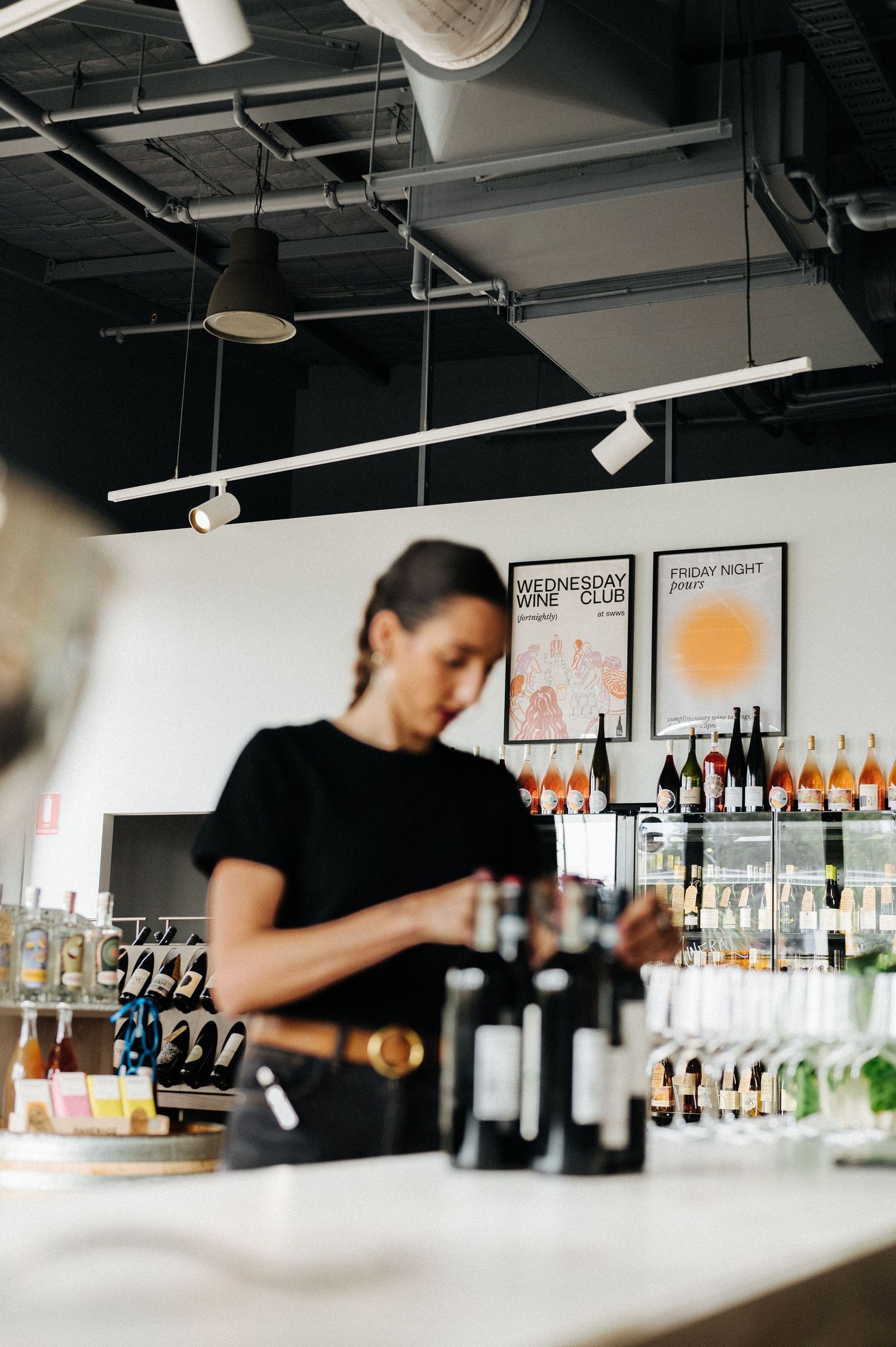 Bar interior with equipment and bottles displayed while staff prepares drinks at counter.