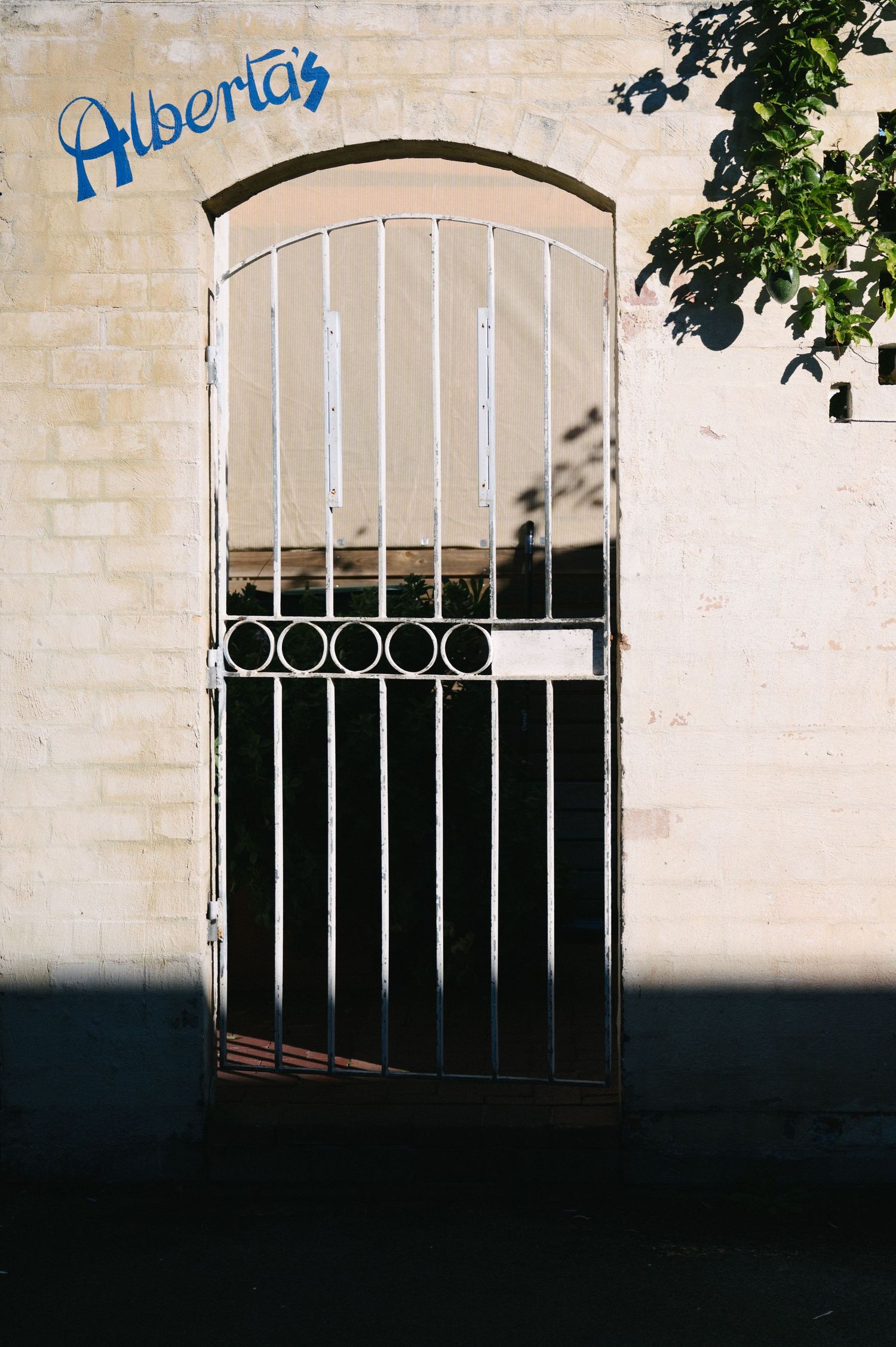 White metal gate entrance with 'Alberta's' text painted above in blue.