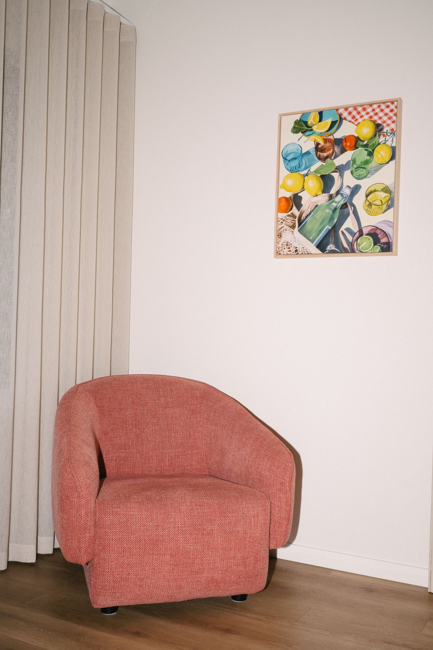 Coral accent chair with colorful abstract artwork displayed on white wall.