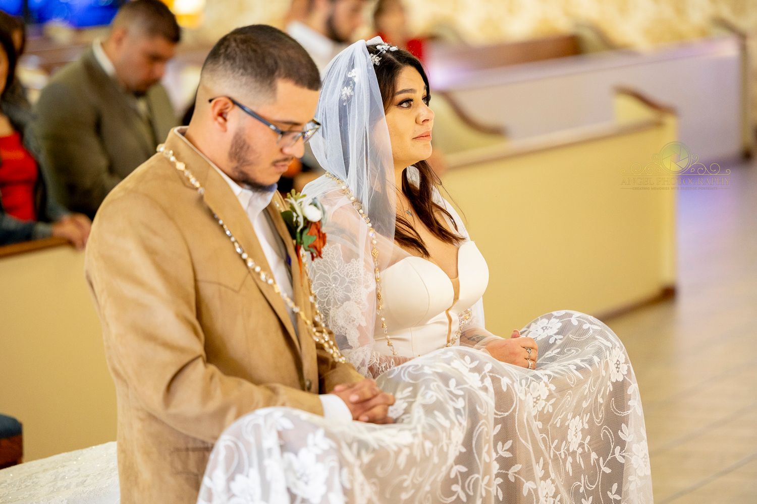 A couple sits together during their wedding ceremony in a church with elegant white lace details.