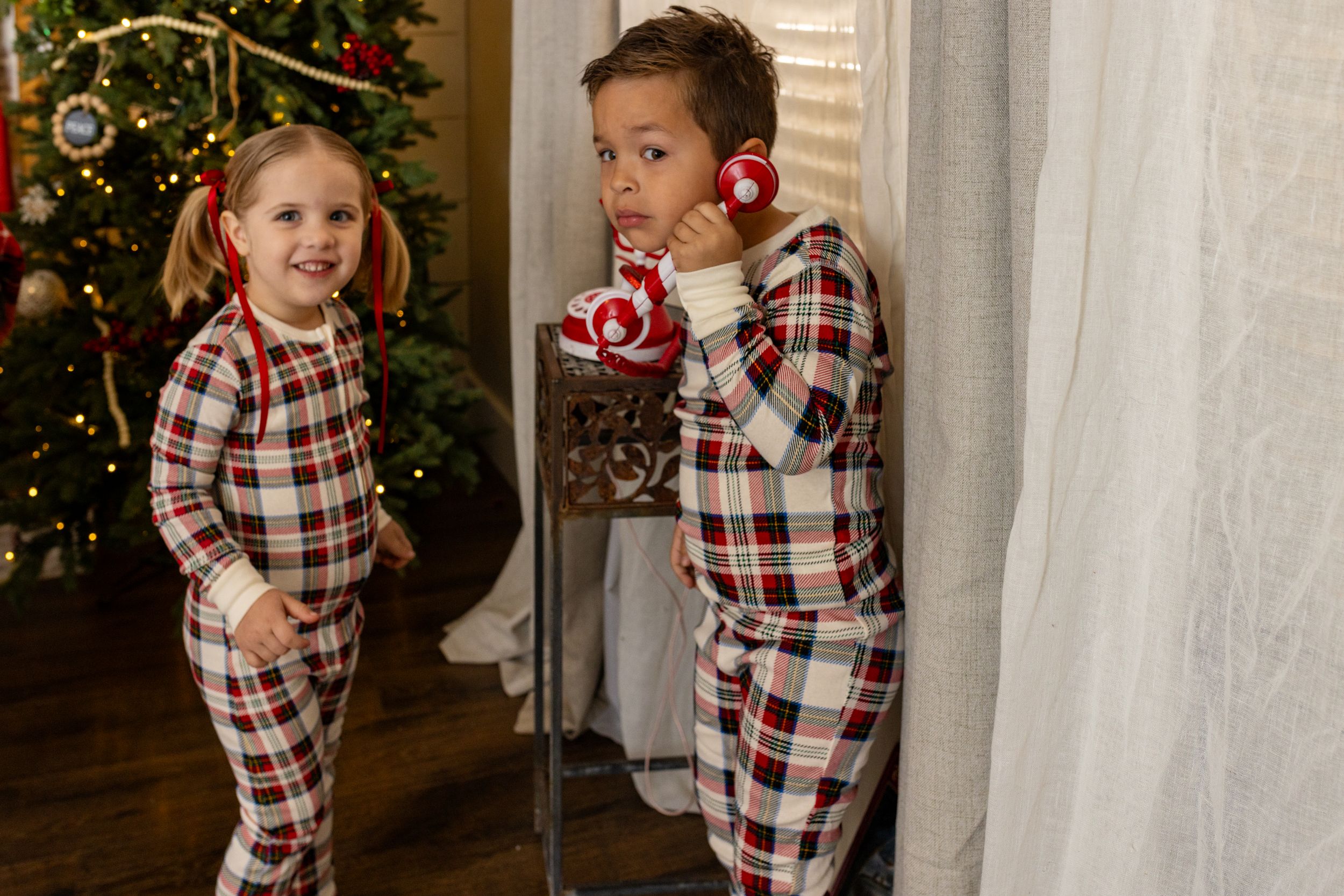 Two young people in matching plaid pajamas playing near a decorated Christmas tree.
30 minute santa session