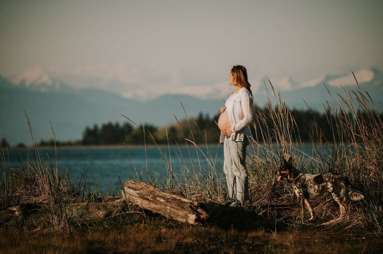 Pregnant woman holding her belly on Vancouver Island beach looking at mountains Maternity Photography by Photographer Soulfull Photographs