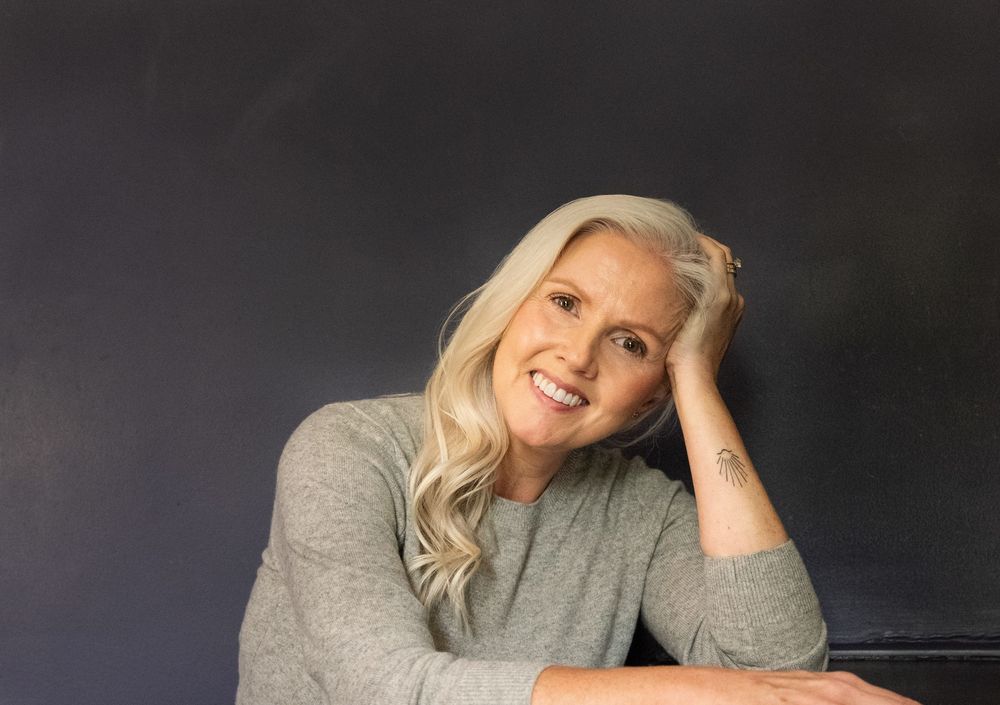 Smiling woman with long blonde hair resting her head on her hand and smiling at the camera