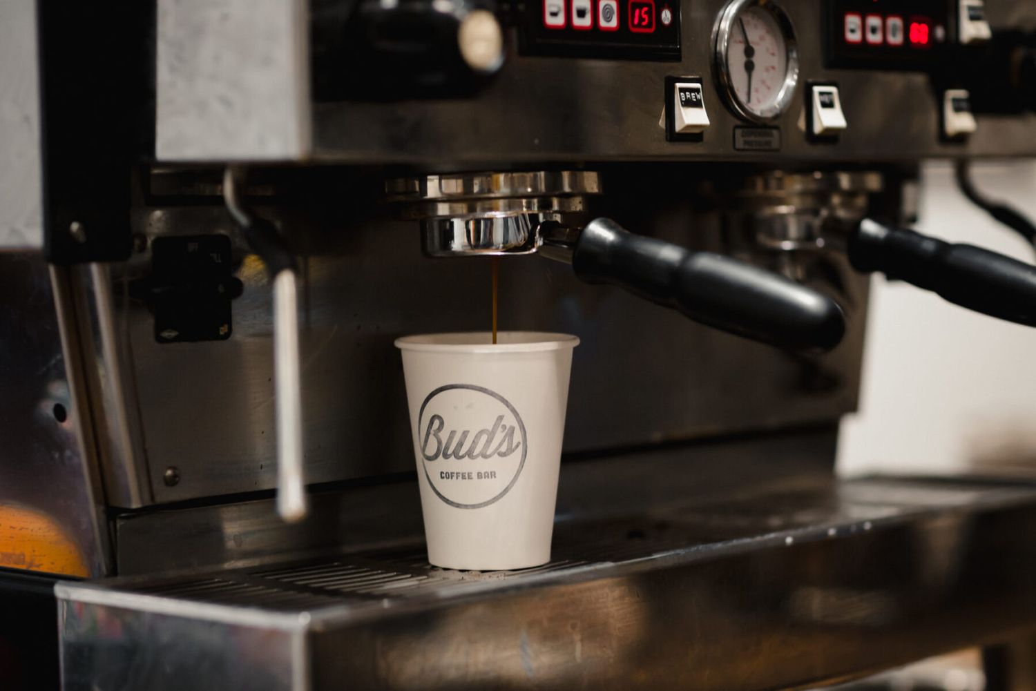Coffee cup with Built logo being filled from espresso machine in dark cafe setting.